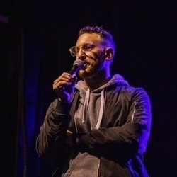 Ahri Findling performing stand-up comedy on stage, known online as theycallmeahri